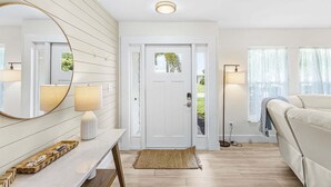 Uma sala de estar moderna com uma porta branca, um espelho redondo, um abajur, um sofá e um tapete pequeno.