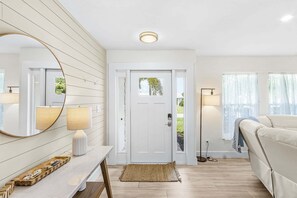 Ein modernes Wohnzimmer mit einer weißen Tür, einem runden Spiegel, einer Stehlampe, einem Sofa und einem kleinen Teppich.