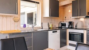 A modern kitchen with a dishwasher, oven, and a dining area with a table and chairs. - 4 Star Holiday Home in Rudkobing (Rudkobing)