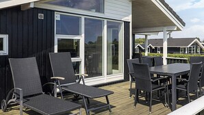 A covered outdoor seating area with chairs and a table, a large sliding glass door, and a view of neighboring houses. - 4 Star Holiday Home in Rudkobing (Rudkobing)