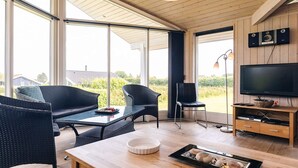 A modern living room with a large TV, wicker furniture, and a dining table with a bowl and tray. - 4 Star Holiday Home in Rudkobing (Rudkobing)