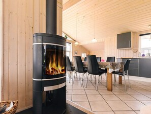 Ein Kaminofen in einem Raum mit Holzwänden, einem Fliesenboden und einem Essbereich mit Stühlen und Tisch.