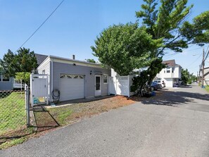 Einbungalow mit Garage, einem eingezäunten Garten und einem Baum davor.