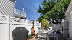 A patio area with a barbecue grill, outdoor table, chairs, and a potted plant. - Charming Single-Family Beach Retreat in the Heart of Ocean City (Ocean City)