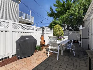 Eine Terrassenfläche mit Grill, Tisch, Stühlen und einem Blumentopf.