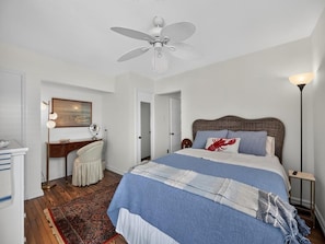 Ein Schlafzimmer mit einem Bett, einem Deckenventilator, einem Schreibtisch und einem Stuhl.