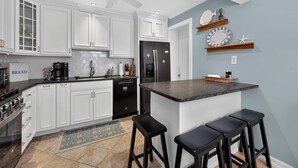 A modern kitchen with white cabinetry, a black refrigerator, a central island with bar stools, and a ceiling fan. - Charming Single-Family Beach Retreat in the Heart of Ocean City (Ocean City)