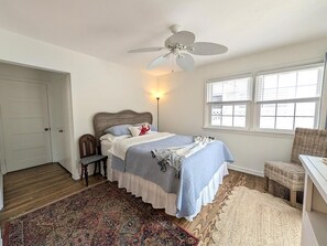 Ein Schlafzimmer mit Bett, Sessel, Deckenventilator, Fenster und Tür.