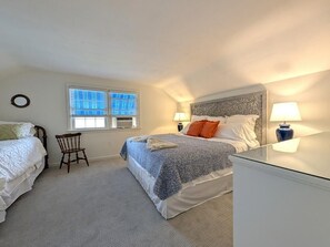 A bedroom with two beds, a chair, a bedside table, a lamp, and a window with blinds.