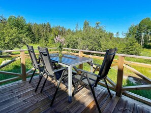 A deck with a table and chairs, surrounded by a wooden railing, overlooking a forested area. - 4 Star Holiday Home in Figeholm (Figeholm)