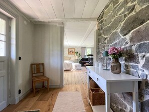 Un pasillo con un banco de madera, una mesa blanca con un florero y una pared de piedra.