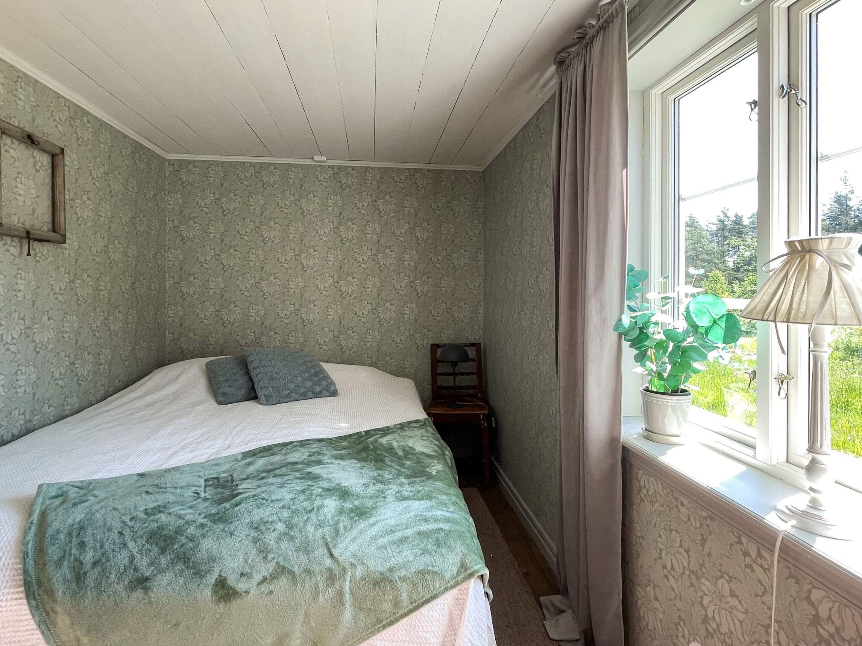Un dormitorio con una cama, una mesita de noche, una lámpara y un ventanal con cortinas.