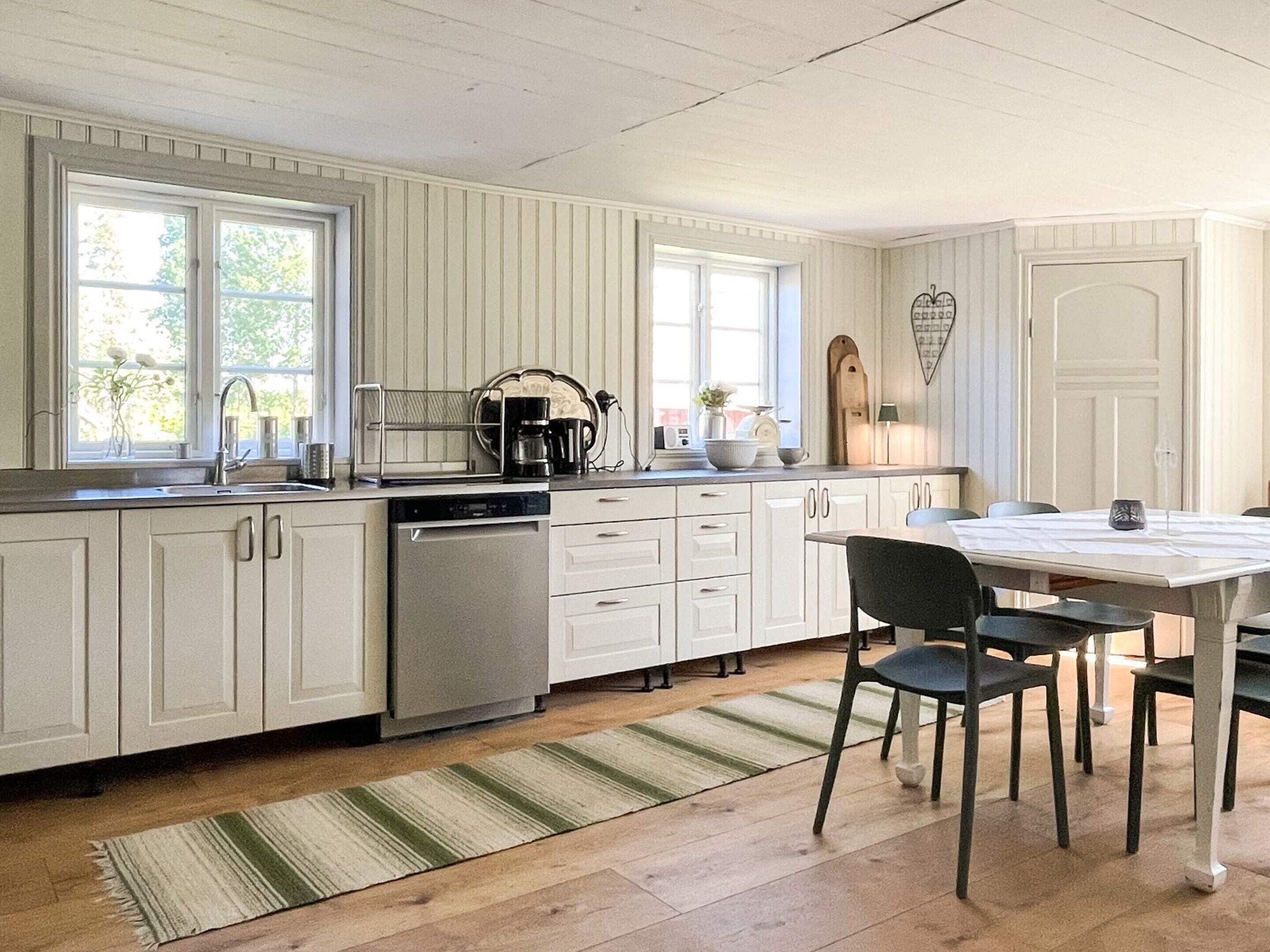 A kitchen with white cabinetry, a dishwasher, a coffee maker, and a dining table with chairs.
