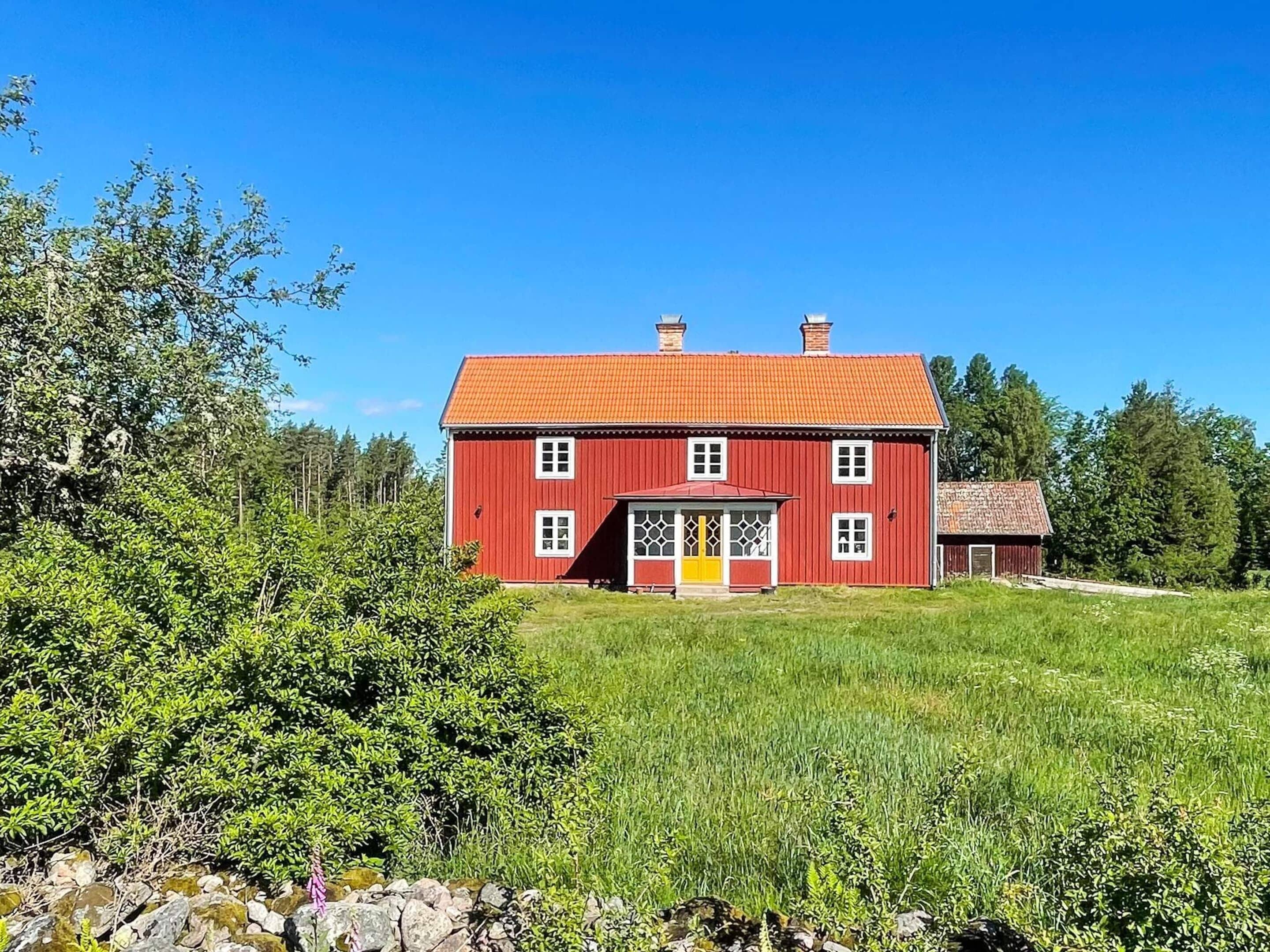 A red two-story house with a red roof, a yellow door, and a small porch.