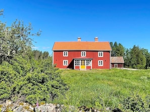 Ein rotes, zweistöckiges Haus mit rotem Dach, einer gelben Tür und einer kleinen Veranda.