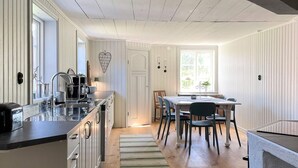 Uma cozinha com ilha central, área de refeições com mesa e cadeiras, e vista pela janela.