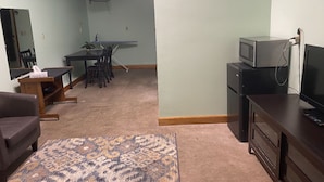 A living room with a sofa, a coffee table, a TV stand, a small refrigerator, and a dining area with a table and chairs. - Cozy 1-bedroom 1-bathroom suite in enchanting Rossford with AC (Rossford)