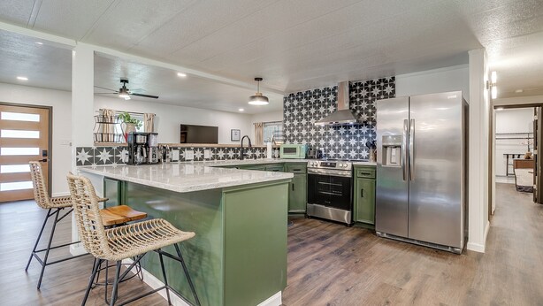 A modern kitchen with a central island, bar stools, a refrigerator, and a stove.