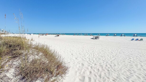 Ein weiter Sandstrand mit blauem Himmel, einigen Strandsonnenschirmen und wenigen Liegestühlen.