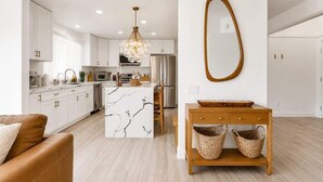 A modern kitchen with white cabinets, a marble island, and a chandelier.
