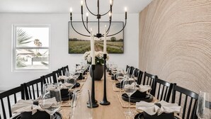 A dining area with a long table set for a meal, a black candelabra, and a framed landscape painting on the wall.
