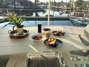 Ein Tisch mit Frühstücksgebäck, einer Zimmerpflanze und Blick auf einen Pool und Gebäude.