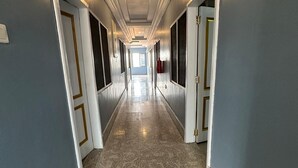 A long, narrow hallway with a tiled floor, doors on both sides, and a ceiling with recessed lighting. - ESTHEMERS ROYAL HOTEL (Kumasi)