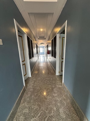 Un long couloir étroit, doté d’un sol carrelé, de portes des deux côtés et d’un plafond équipé de luminaires encastrés.