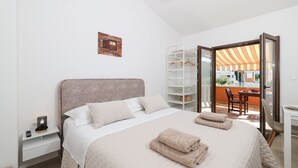 Quarto com cama, mesa de cabeceira e vista para uma varanda externa.