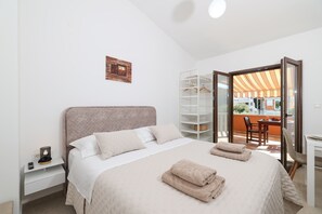 A bedroom with a bed, bedside table, and a view of an outdoor balcony. - Studio apartment Gabriella (Sukošan)