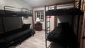 A room with bunk beds, a wooden chair, a small table, a lamp, and a window.
