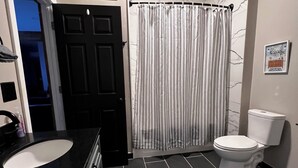 A bathroom with a black sink, white toilet, and a striped shower curtain.