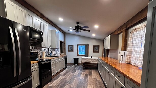A modern kitchen with a black refrigerator, microwave, and oven, wooden flooring, and a ceiling fan.