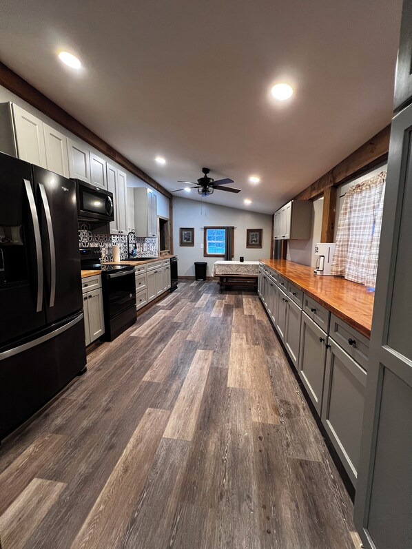 A modern kitchen with a black refrigerator, microwave, and oven, wooden flooring, and a ceiling fan.