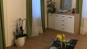 Ein Zimmer mit Holzboden, einem kleinen gelben Stuhl, einer Topfpflanze, einem Schrank und grünen Vorhängen.