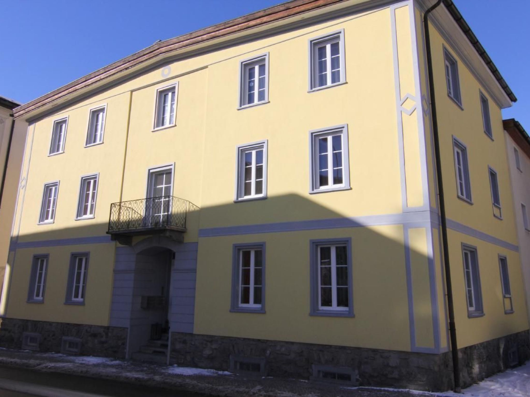 Ein gelbes Gebäude mit vielen Fenstern und einem Sockel aus Stein.