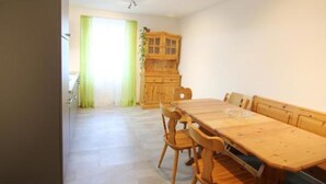 Ein Essbereich mit Holztisch und -stühlen, einem Holzschrank und Blick auf einen grünen Vorhang und ein Fenster.