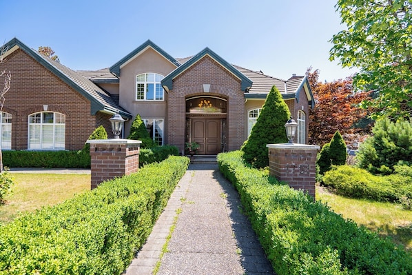 A two-story house with a brick facade, a central entrance with a door, and a pathway leading to the front.