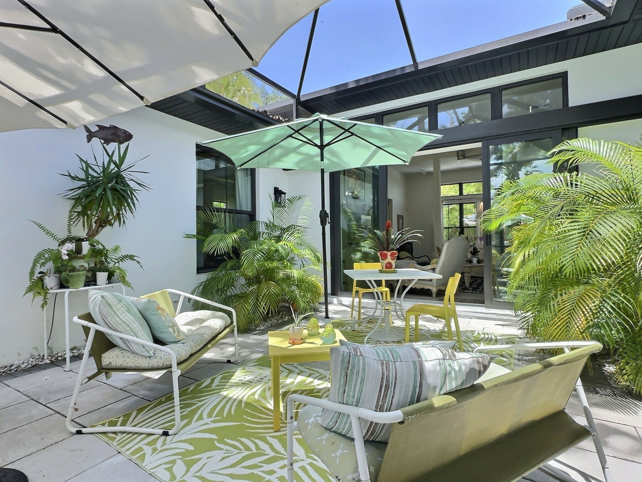 Un área de patio al aire libre con un conjunto de mobiliario, incluyendo un sofá y sillones, una mesa y un paraguas verde.