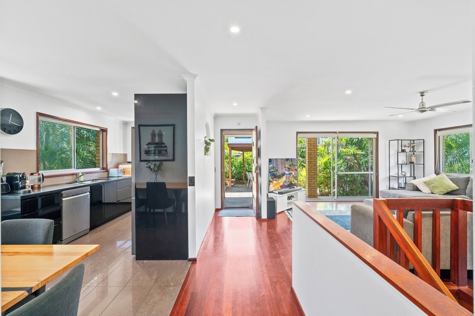 A modern kitchen with a dining area, a staircase, and a view of greenery outside.