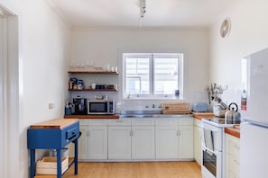 A compact kitchen with white cabinets, a wooden countertop, a microwave, a kettle, and a window with blinds.