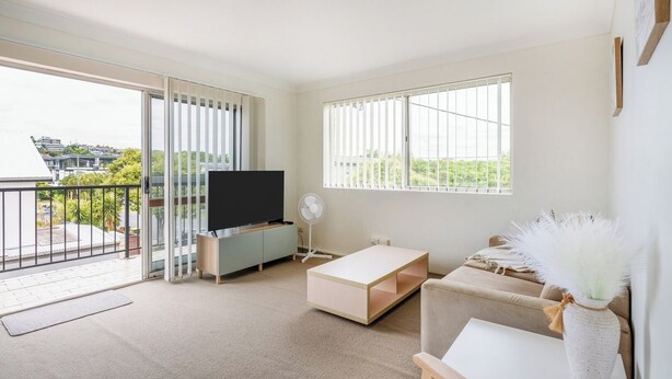 Een moderne woonkamer met een flatscreen televisie, een bank, een salontafel en een balkon met uitzicht op gebouwen en groen.