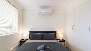 Een hotelkamer met een bed, twee bedlampen, een raam met zonwering, een airconditioner en een kledingkast.