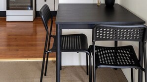 Een eethoek met een zwarte tafel, twee zwarte stoelen, een potplant, een gasfornuis, een magnetron en een klok aan de muur.