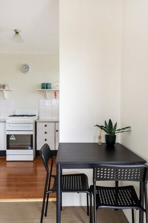 A dining area with a black table, two black chairs, a potted plant, a gas stove, a microwave, and a clock on the wall. - Quiet and Cosy Bulimba Escape (Bulimba)