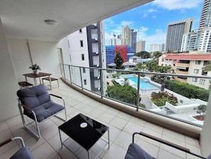 Ein Balkon mit Blick auf einen Swimmingpool, hohe Gebäude und einen Blumentopf.