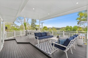 A covered outdoor deck with a white railing, a blue sofa, white chairs, and a patterned rug.
