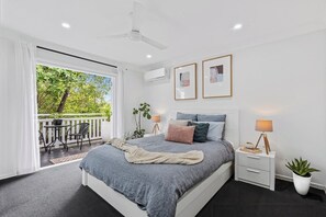A bedroom with a bed, bedside tables, a lamp, a potted plant, and a balcony with a table and chairs.