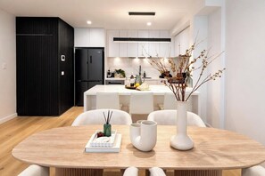 Eine moderne Küche mit weißen Schränken, einem schwarzen Kühlschrank und einem Essbereich mit Holztisch und Stühlen.