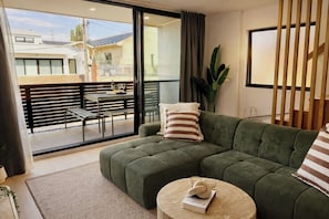Ein modernes Wohnzimmer mit einem Ecksofa, einem runden Couchtisch und Blick auf einen Balkon mit Gartenmöbeln.